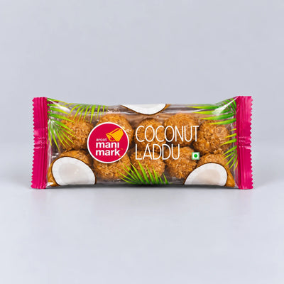 A packaged snack bar of Anand Mani Mark Coconut Laddu, featuring brown coconut-coated sweets visible through a clear wrapper with pink ends and coconut graphics, on a light gray background.