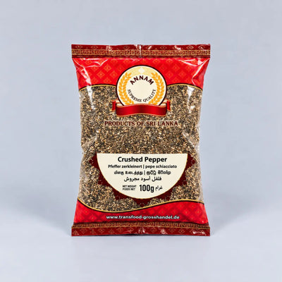 A 100g bag of Annam Crushed Pepper (pepper schiacciato) from Products of Sri Lanka, featuring a red and gold patterned packaging with a clear window showing the ground black pepper inside, set against a light gray background.