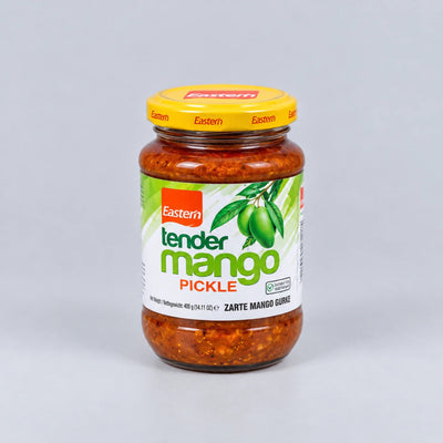 A glass jar of Eastern Tender Mango Pickle with a yellow lid and a white label featuring green mango graphics, set against a neutral gray background.
