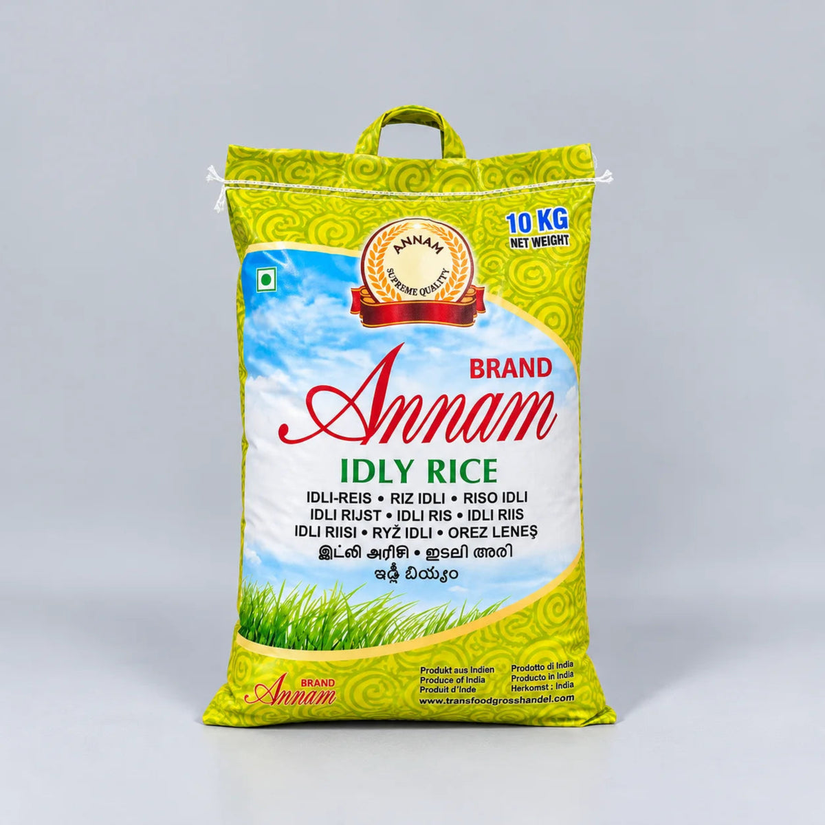 A 10 kg bag of Annam Brand Idly Rice, featuring a bright yellow-green bag with a blue sky and green grass illustration, set against a neutral gray background.