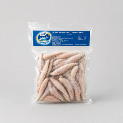 A clear plastic bag of frozen anchovies, labeled 'Kool Delight Frozen Anchovy Ml Cleaned Large', containing several pale pinkish-beige frozen anchovies, set against a neutral light gray background.