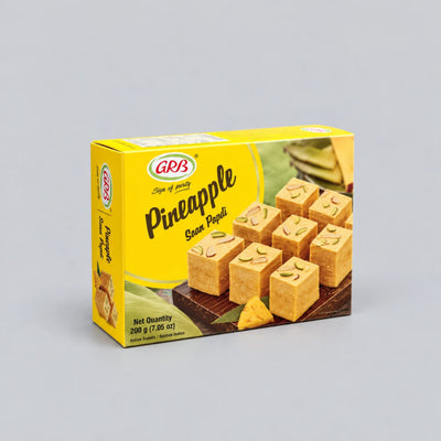 A box of GRA Pineapple Soan Poodi sweets, featuring a bright yellow packaging with an image of the golden-brown square sweets decorated with sliced pineapple on top, set against a neutral gray background.