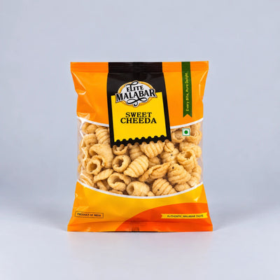 A bag of Elite Malabar Sweet Cheeda pasta on a light gray background. The packaging is bright orange and yellow with a black central label, and a clear window shows the spiral-shaped golden-brown pasta inside.