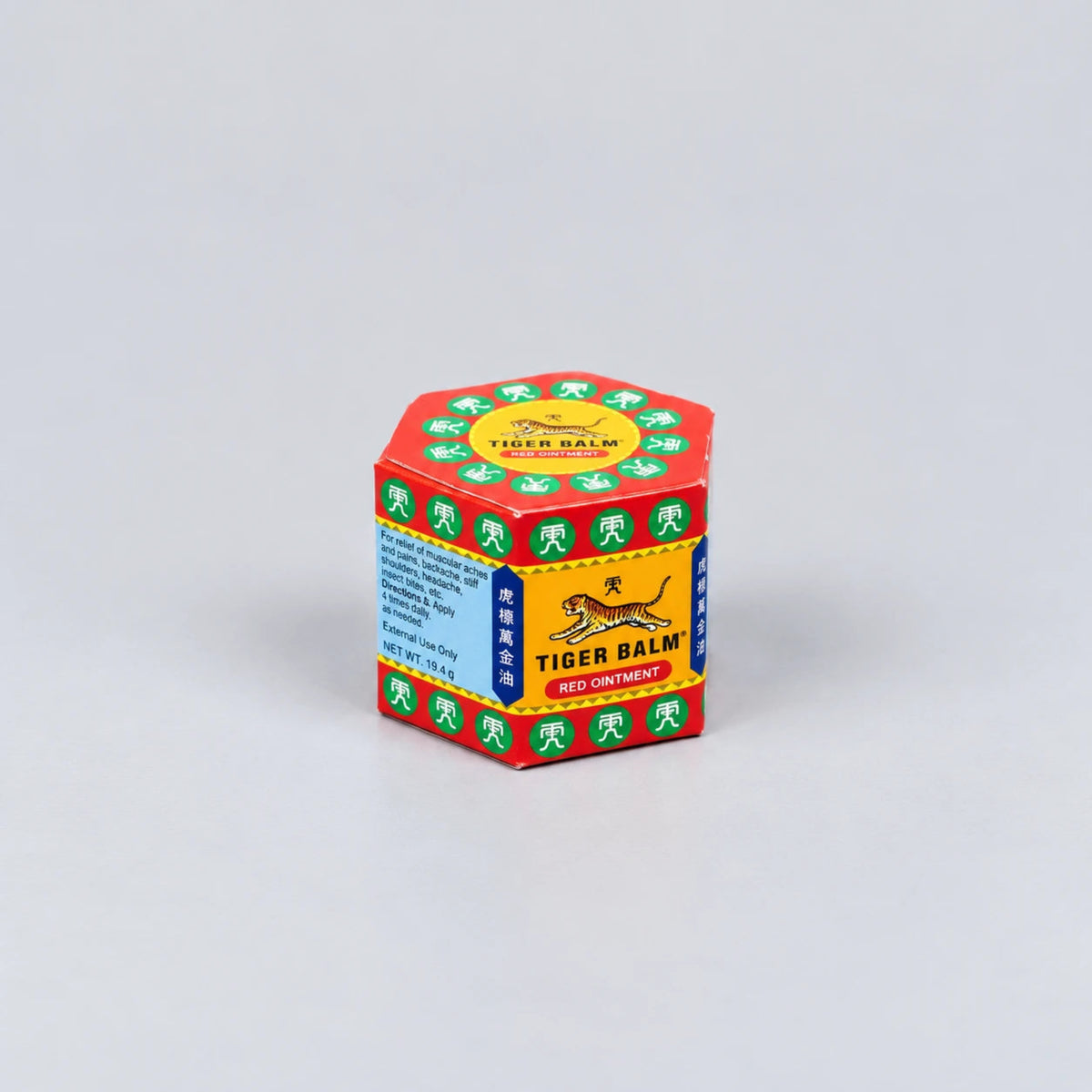 A hexagonal box of Tiger Balm Red Containment, featuring its signature red, yellow, green, and blue packaging with the brand's tiger logo, set against a plain light gray background.