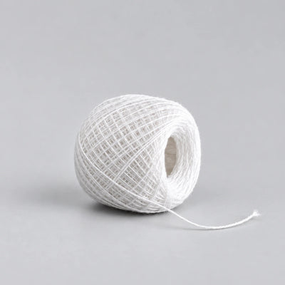 A ball of white twine or thread with a short tail extending to the right, photographed on a clean light gray studio background.