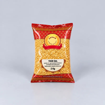 A 2 kg bag of Annam Premium Quality Tour Dal (mung bean) in a red and gold patterned package with a clear window showing the yellow-beige mung beans inside, set against a light gray background.