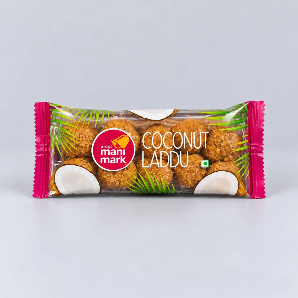 A packaged snack bar of Anand Mani Mark Coconut Laddu, featuring brown coconut-coated sweets visible through a clear wrapper with pink ends and coconut graphics, on a light gray background.