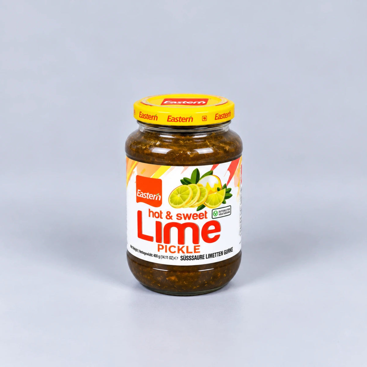 A glass jar of Eastern brand hot & sweet lime pickle, featuring a yellow lid and a white label with red and green text and lime illustrations, set against a neutral gray background.