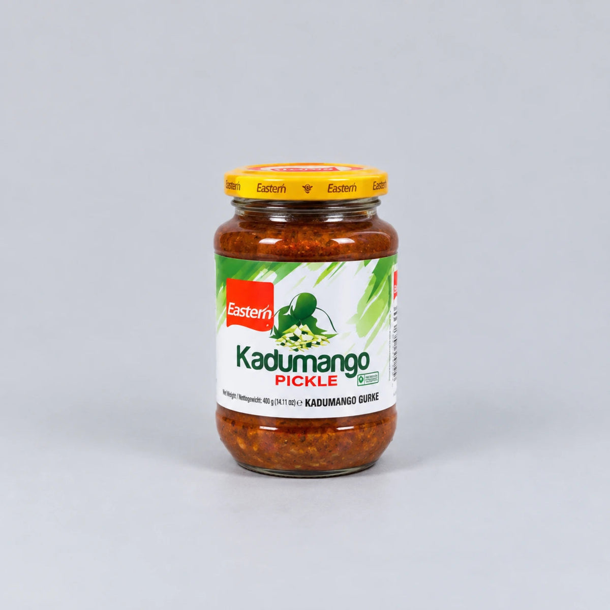 A glass jar of Eastern Kadumango Pickle (Kadumango Guri) with a yellow lid and a white label featuring green and red branding, set against a plain light gray background.