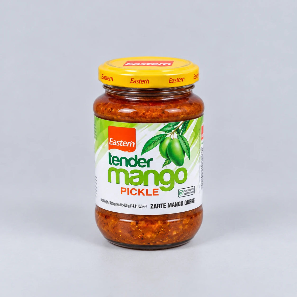 A glass jar of Eastern Tender Mango Pickle with a yellow lid and a white label featuring green mango graphics, set against a neutral gray background.