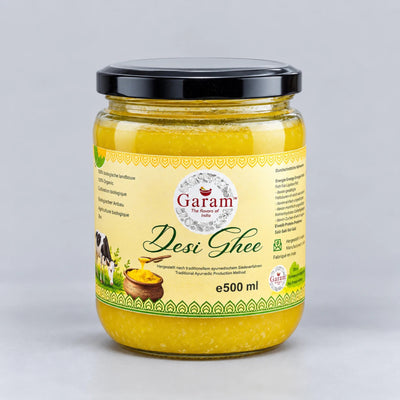 A 500 ml glass jar of Garam Desi Ghee with a black lid and a cream-colored label, set against a neutral light gray background.