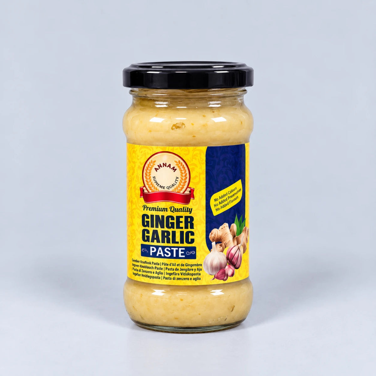 A glass jar of Manam Premium Quality Ginger Garlic Paste, featuring a yellow and blue label with garlic illustrations, sealed with a black lid on a light gray background.