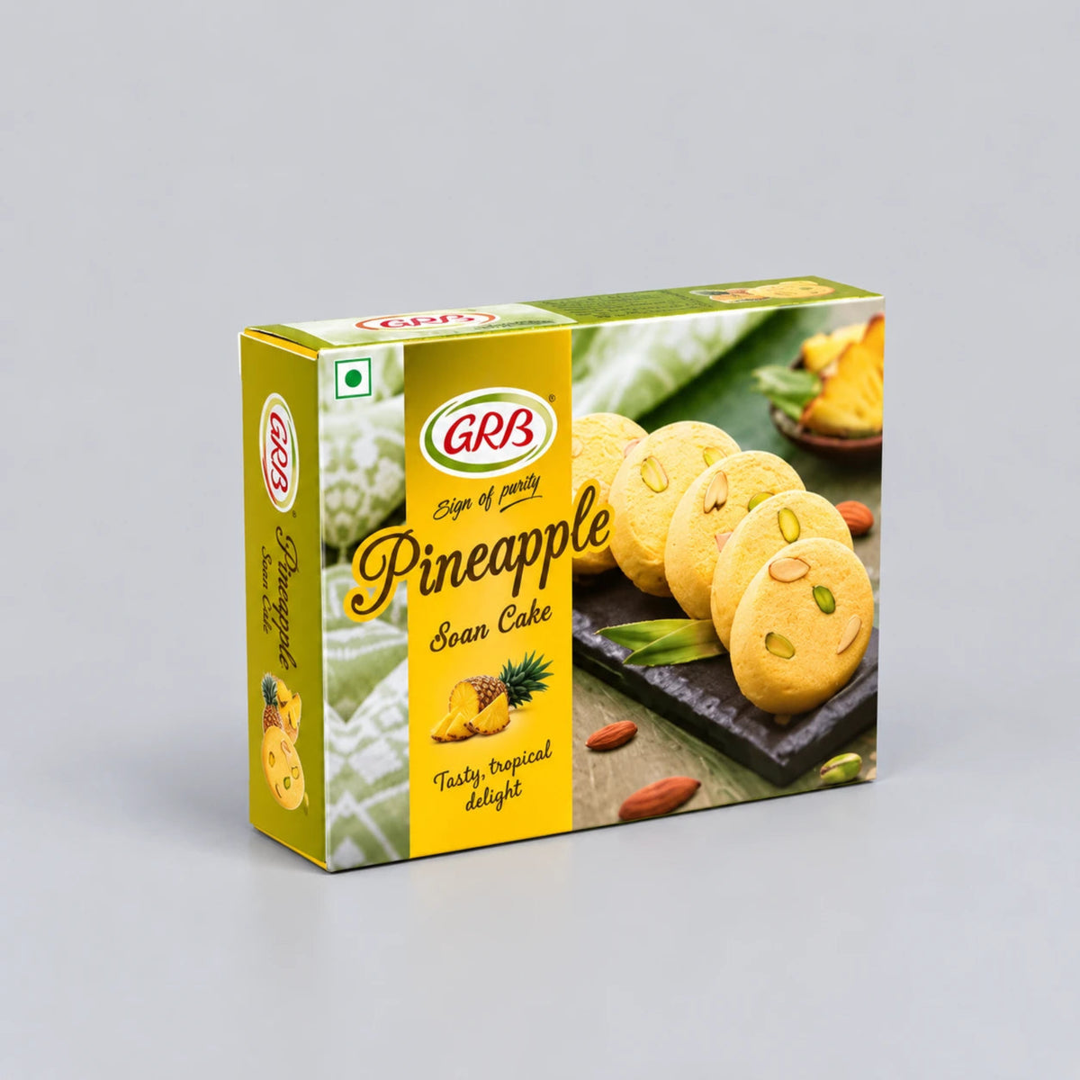 A boxed food product labeled GRB Pineapple Sean Cake, shown in a rectangular retail box with yellow and green packaging and a photo of round sponge cakes on the front, photographed on a light gray studio background.