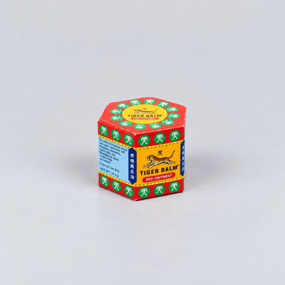 A hexagonal box of Tiger Balm Red Containment, featuring its signature red, yellow, green, and blue packaging with the brand's tiger logo, set against a plain light gray background.